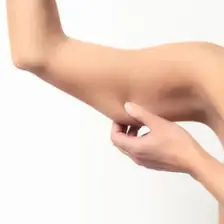 A close-up shot of a woman pinching the skin on her upper arm, concern about loose skin woman demonstrating concern about loose skin or arm fat.