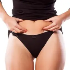 A close-up shot of a woman's torso, with her hands gently pinching the skin on her lower abdomen Close-up of a woman's torso, hands pinching her stomach fat